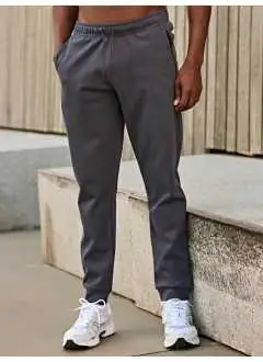 60% cotone 40% popliestere. Pantaloni sportivi in interlock, con elastico e coulisse in vita, due tasche frontali con zip con cordoncino, polsino nello stesso tessuto.